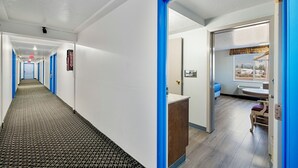Pasillo de hotel con puertas de marco azul, un letrero de salida de incendios y una recepción con vista al exterior.