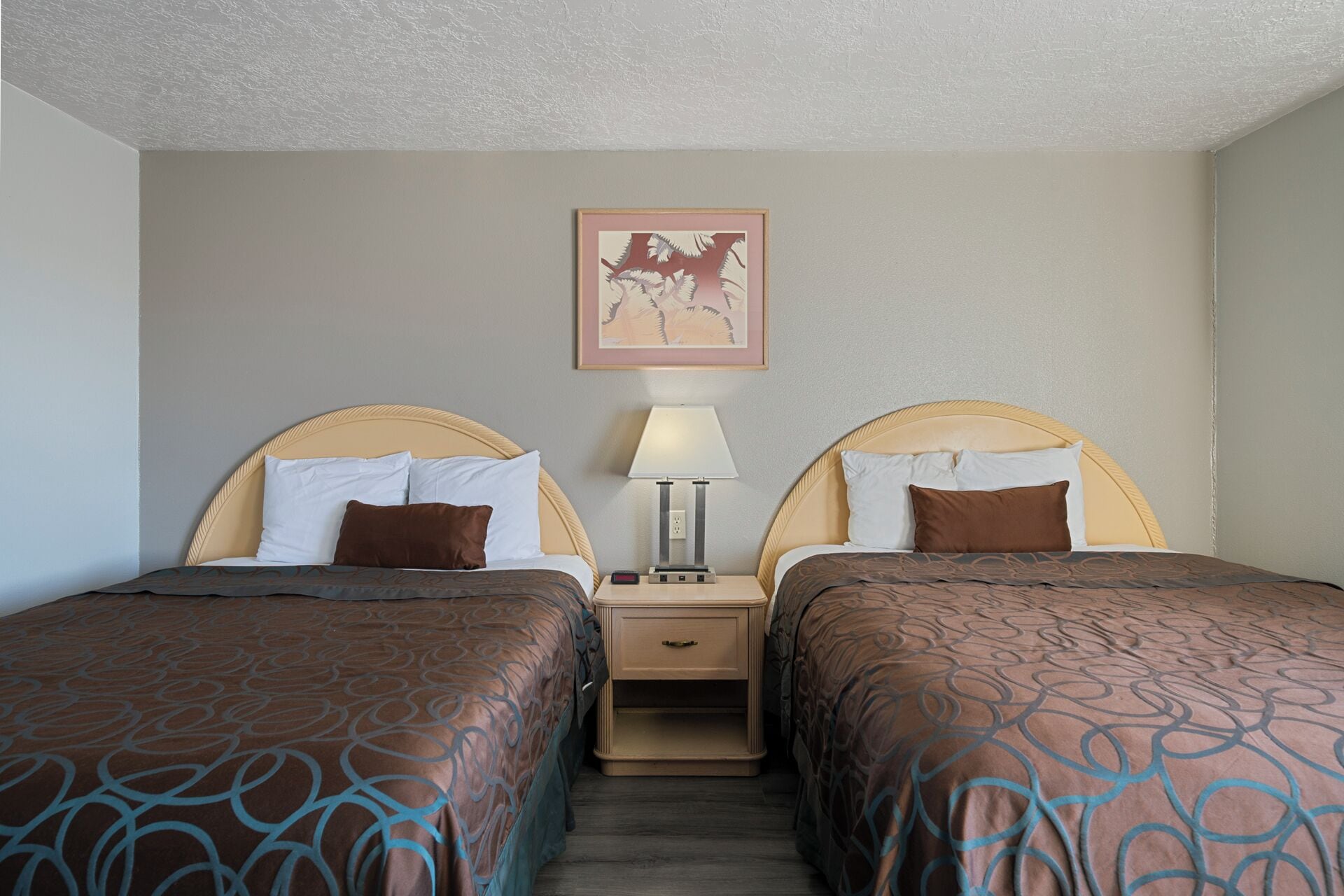 A hotel room with two beds, a nightstand with a lamp, and a framed picture on the wall.