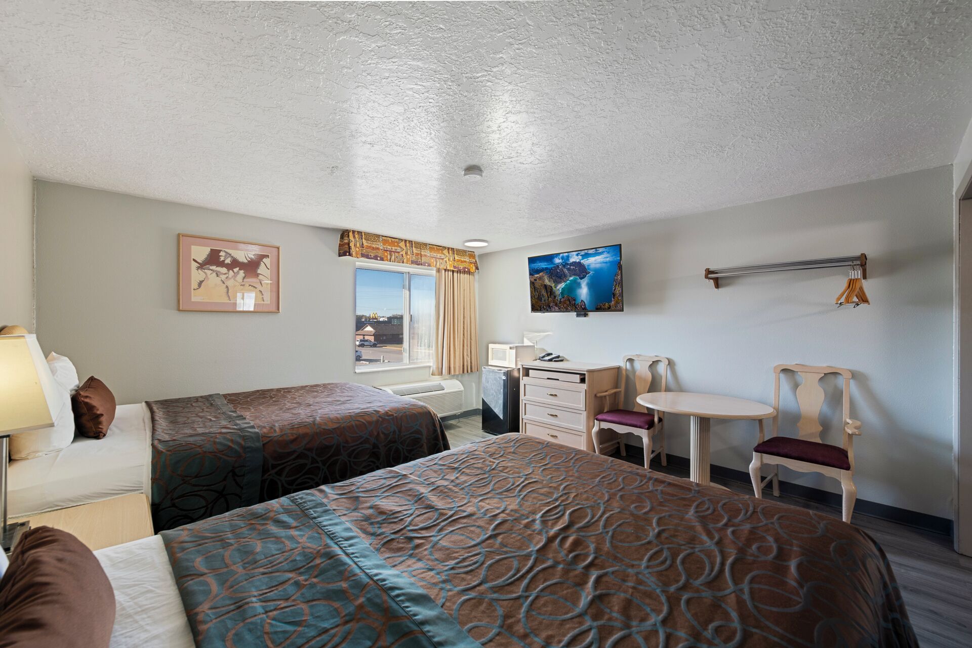 A hotel room with two beds, a desk, a chair, a TV, and a window with curtains.