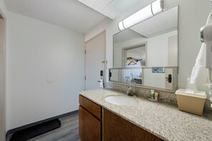 A bathroom with a white sink, wooden cabinets, a mirror, and a towel dispenser.