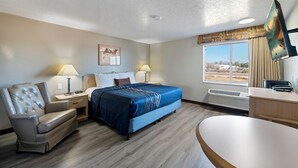 Una habitación de hotel con una cama, un sillón de cuero, un escritorio con una computadora y un ventanal con vistas.