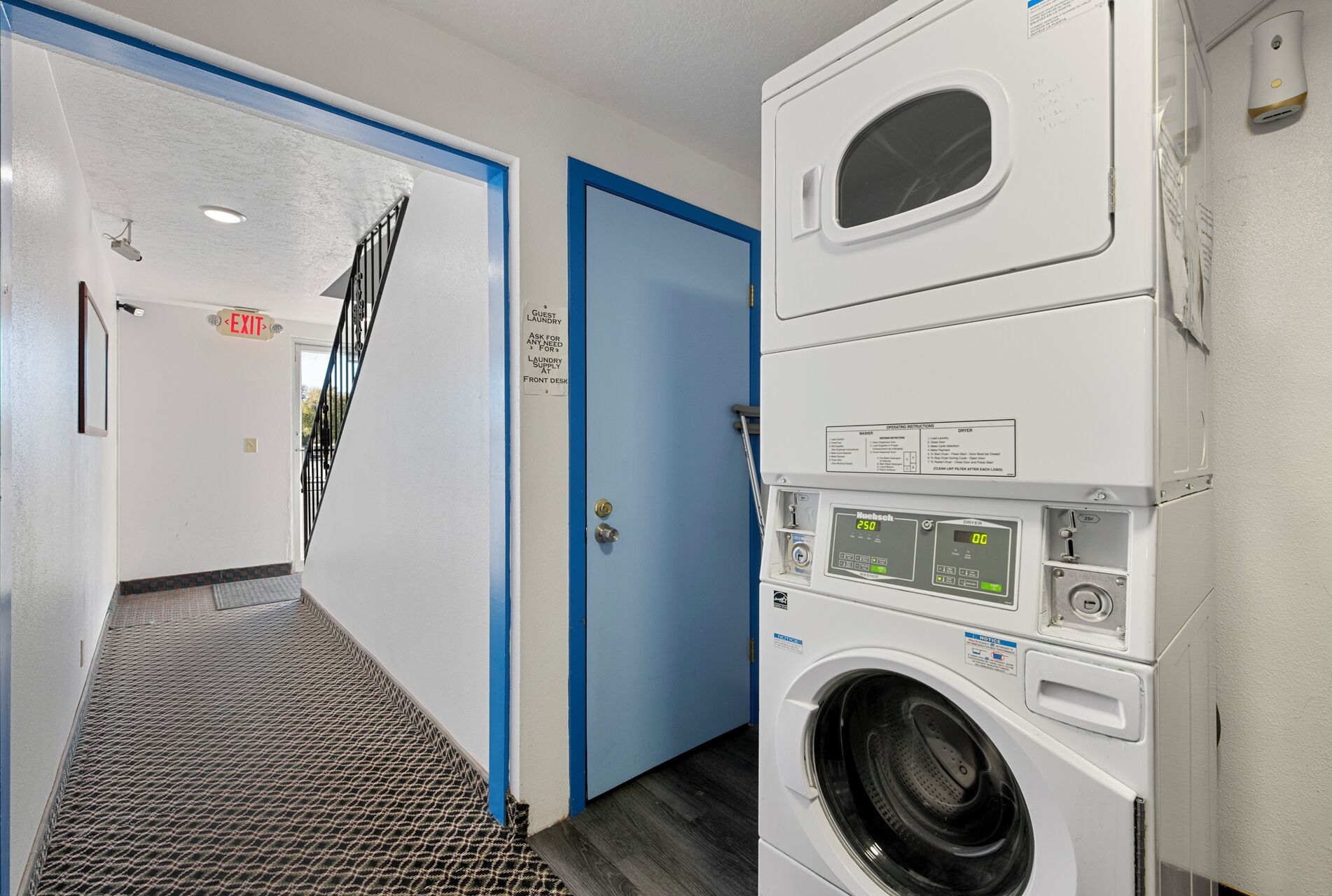 Une buanderie avec un comptoir d’accueil, une porte bleue et un sèche-linge fixé au mur.
