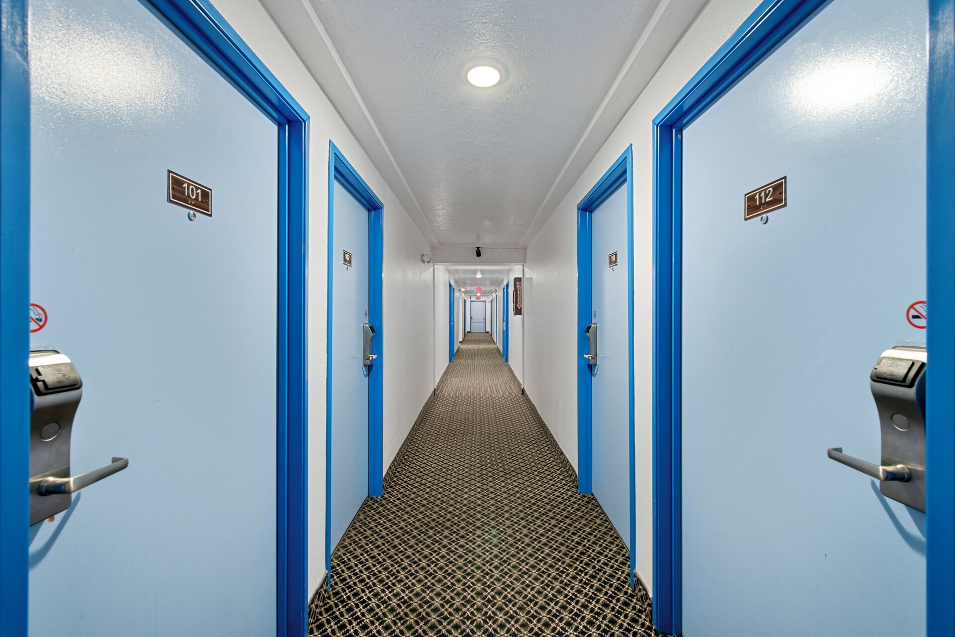 Pasillo de hotel con puertas azules, números 101 y 112, que conducen a las habitaciones.