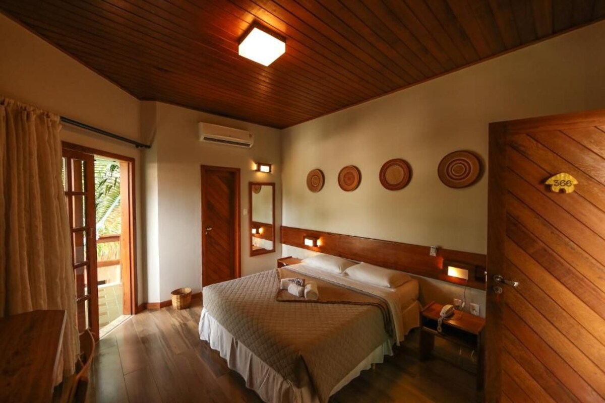 Un dormitorio con paneles de madera, una cama, mesitas de noche, un espejo y una puerta con placa de identificación.
