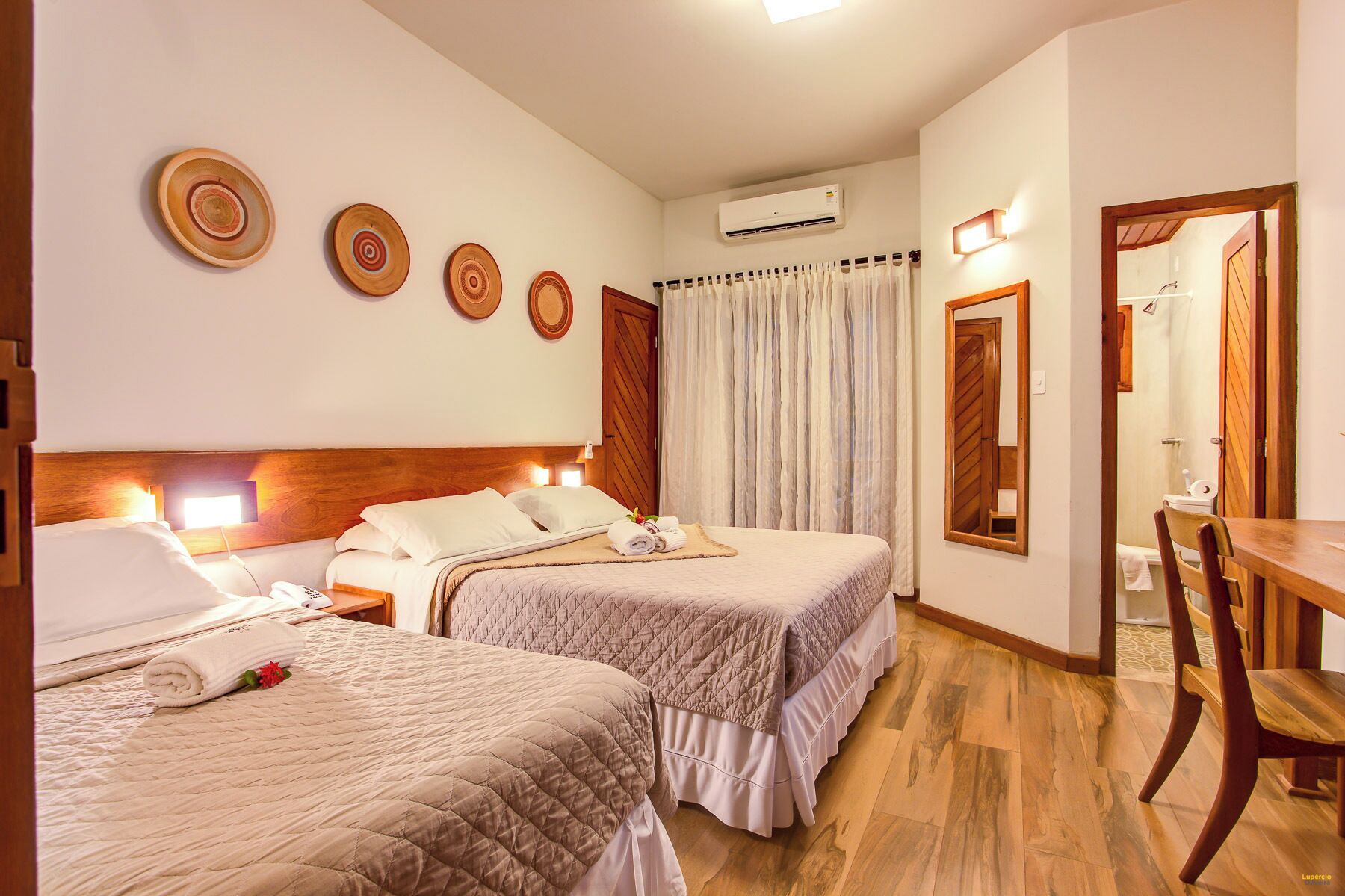 A hotel room with two beds, a wooden headboard, a desk, a chair, a mirror, and a window with curtains.