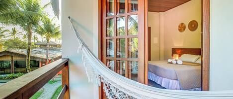 A hammock attached to a balcony railing, overlooking a bed with a wooden headboard and a nightstand.