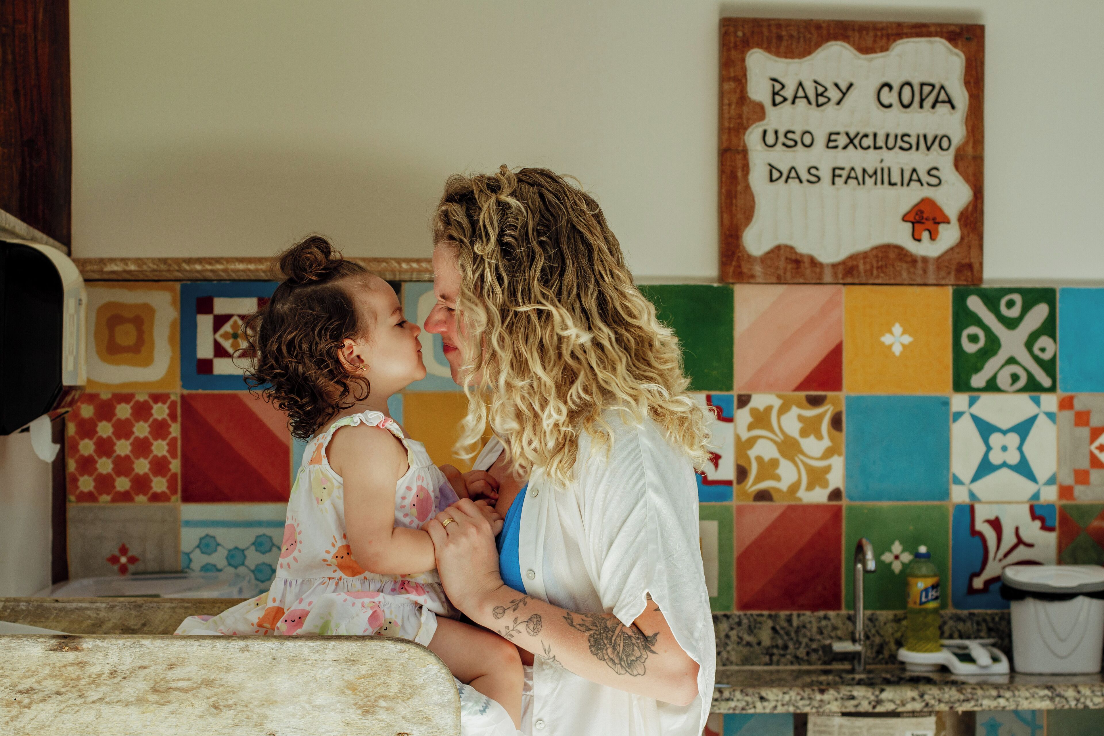 A person holding a child in a room with colorful tiles on the wall and a sign that reads 'BABY COPA USO EXCLUSIVO DAS FAMILIAS'.