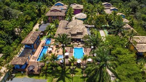 Vista aérea de un complejo turístico con varias edificaciones, una piscina central y palmeras circundantes.