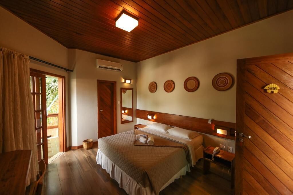 A wooden-paneled room with a bed, bedside table, and a door with a number plate.