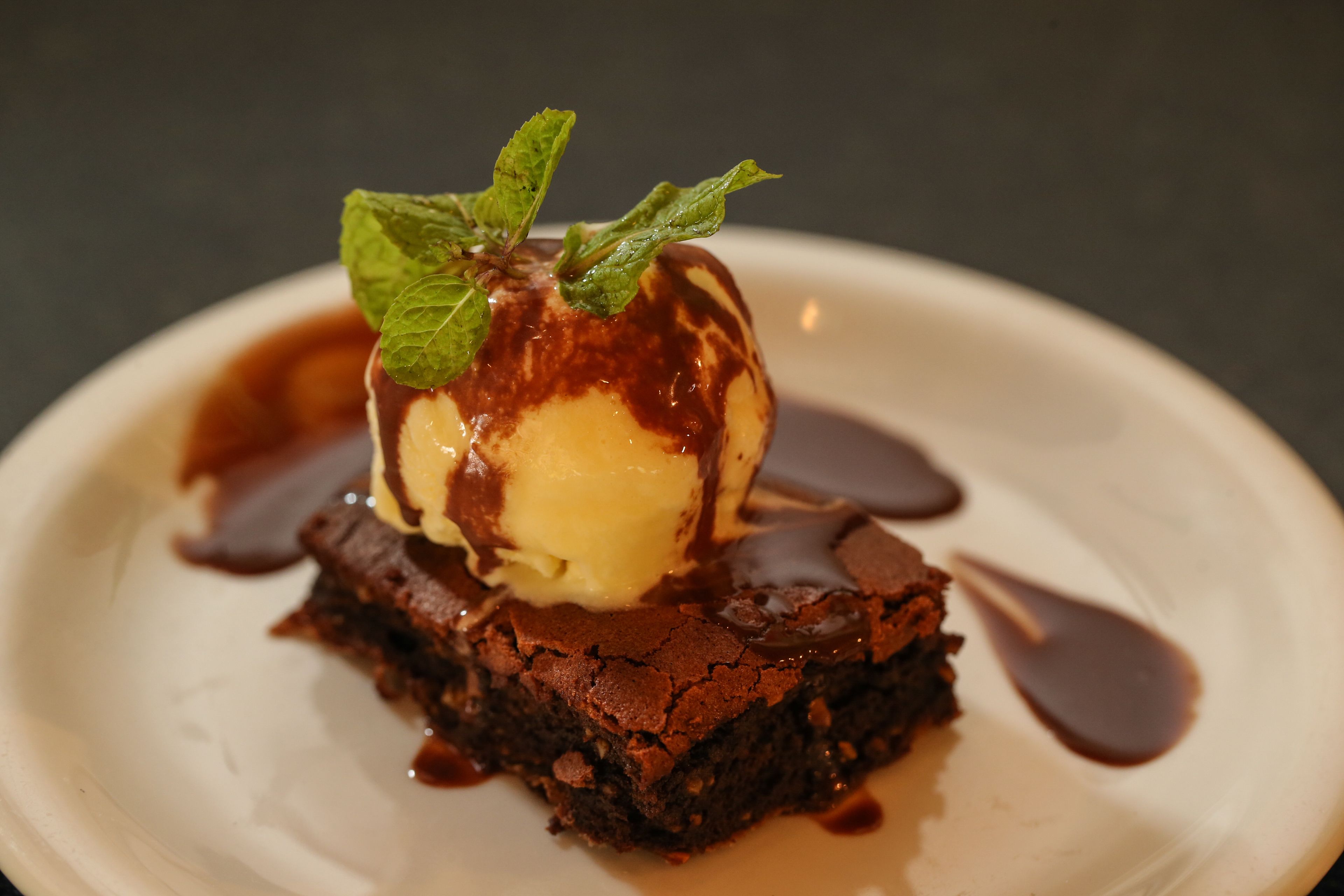 Un postre con una bola de helado encima, adornado con una hoja de menta y cubierto con salsa de chocolate.