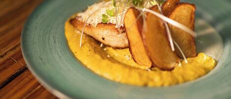 A plate of food with a piece of chicken, potato slices, and a yellow sauce.