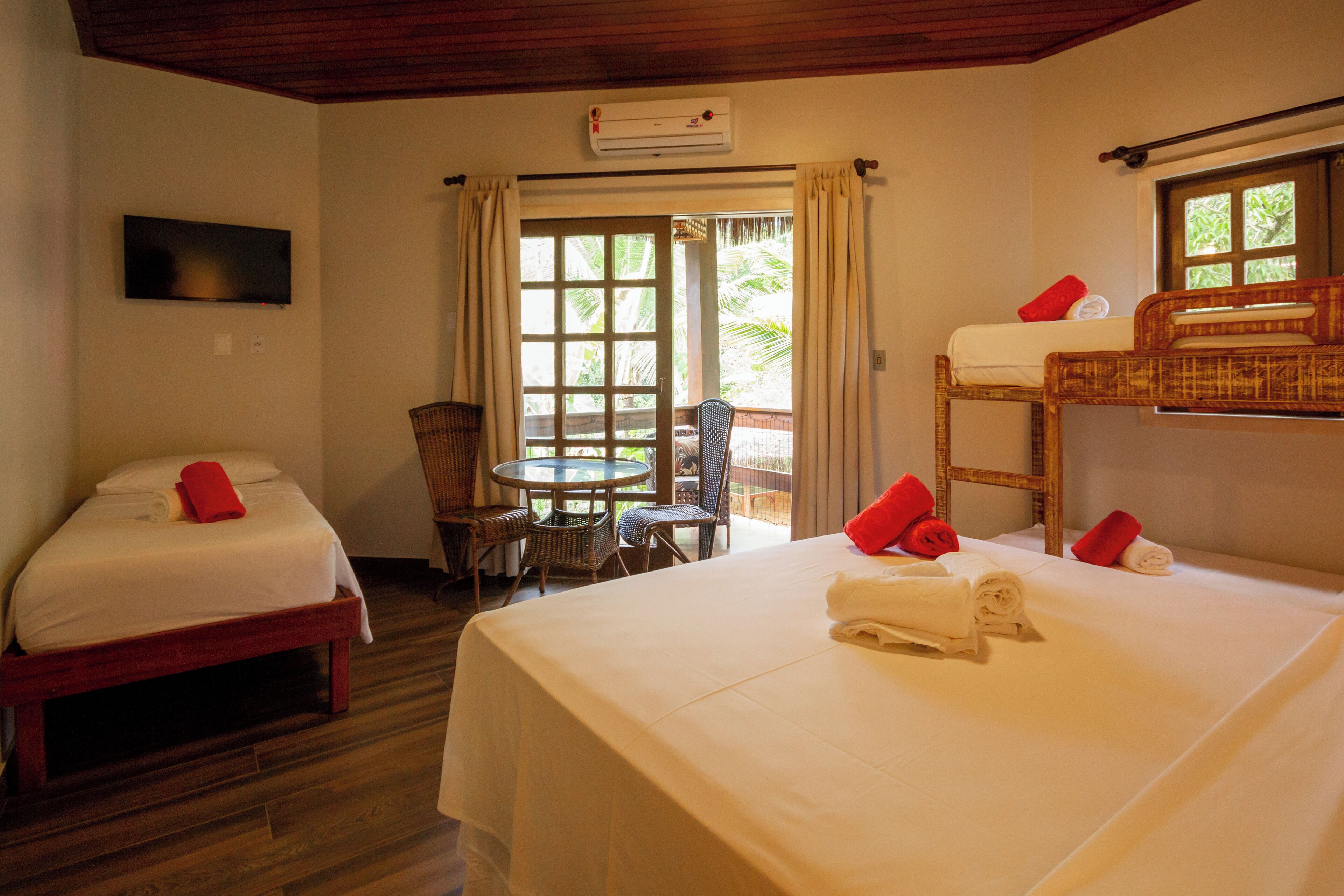 Une chambre d’hôtel avec deux lits simples, un lit superposé, une télévision, une table avec des chaises et une fenêtre avec des rideaux.