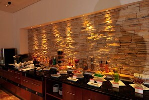 A buffet area with a stone wall backdrop, various food items, and a coffee machine. - Parkcity Everly Hotel (Bintulu)