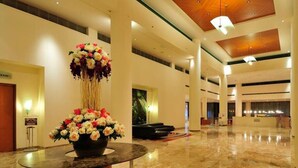 Un vestíbulo amplio con piso de mármol, un arreglo floral central y una recepción al fondo.