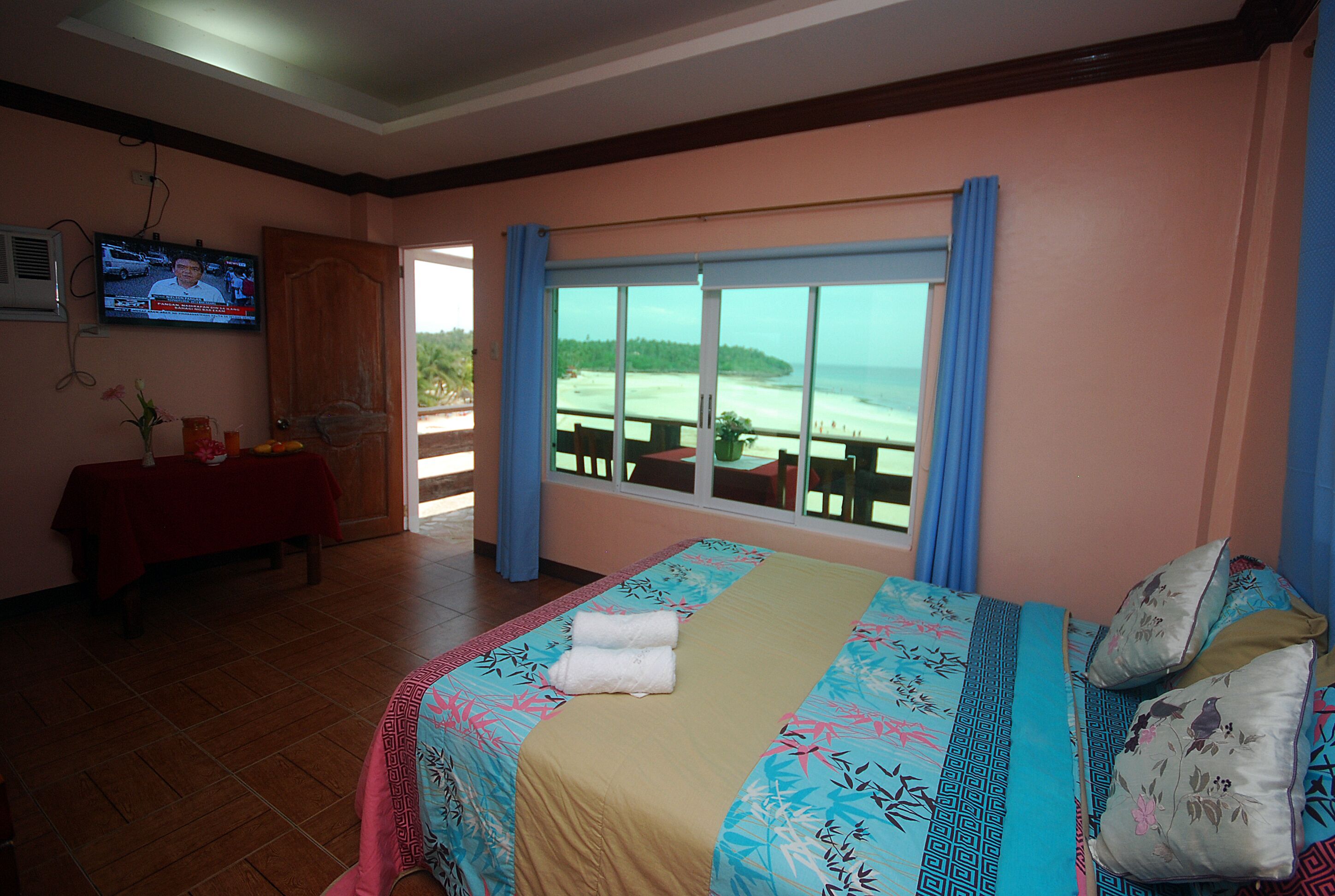 Habitación de hotel con cama, televisión, una mesa con mantel rojo y vistas a la playa.
