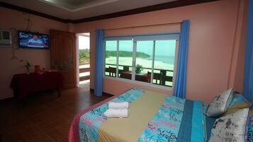 Habitación de hotel con cama, televisión, una mesa con mantel rojo y vistas a la playa.