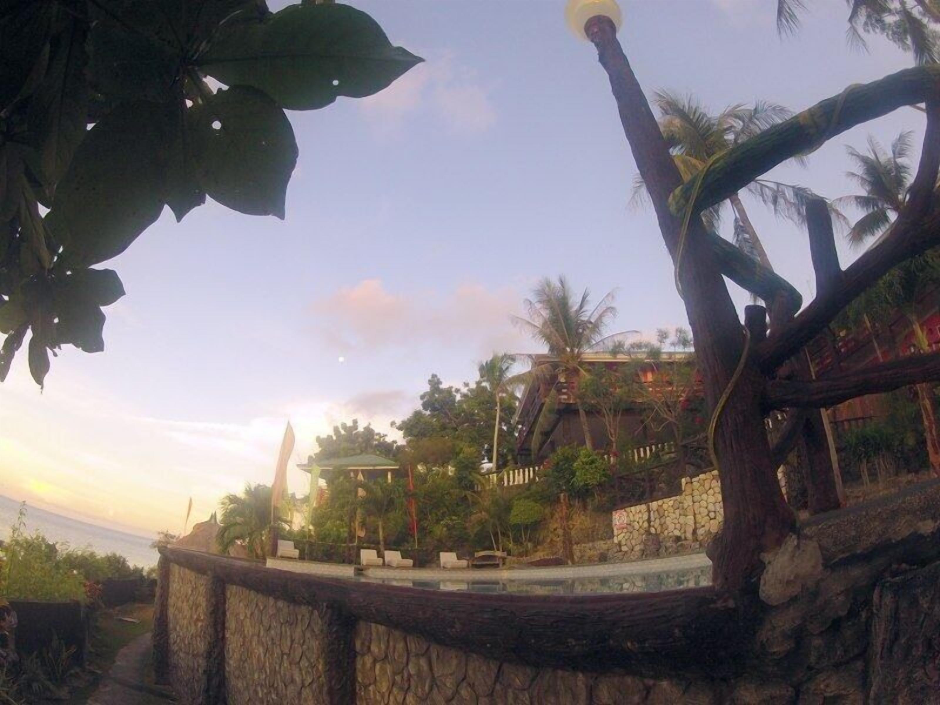 A resort with a stone pathway leading to a pool area, surrounded by palm trees and a view of the ocean.