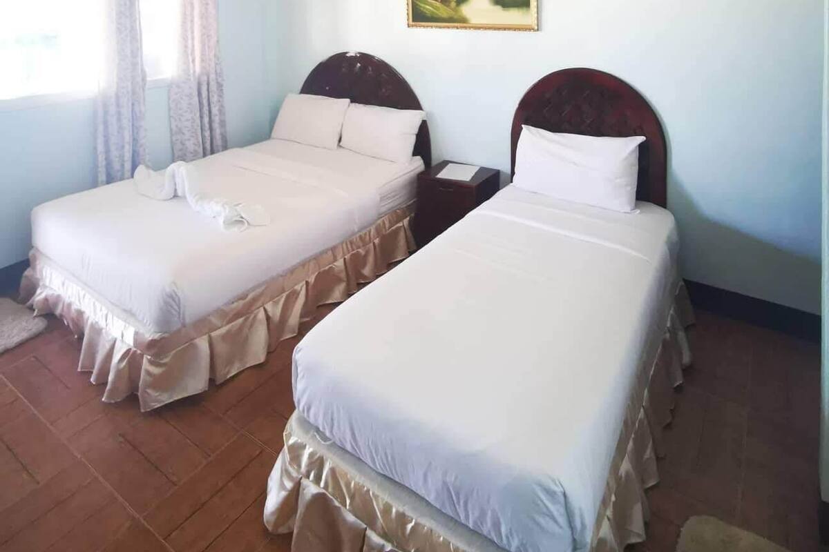 Ein Hotelzimmer mit zwei Einzelbetten, einer Deckenleuchte, einem Bild an der Wand und einem Fenster mit Vorhängen.