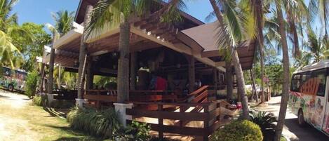 A wooden structure with a covered porch, surrounded by palm trees and greenery.