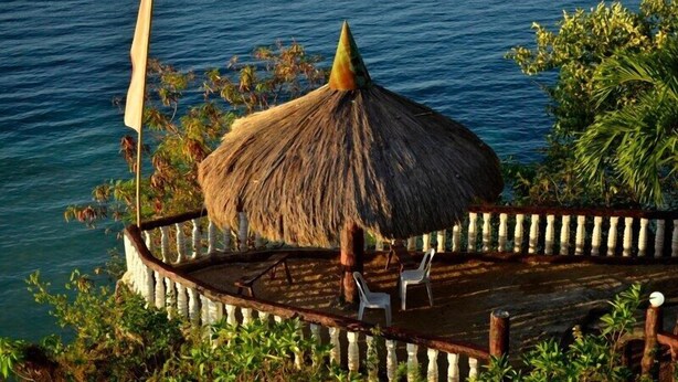 A thatched-roof structure with two white chairs, surrounded by a wooden deck and railing, overlooking a body of water. - Santiago Bay Garden & Resort (San Francisco)