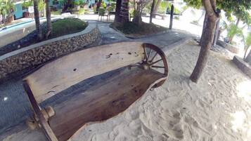 A wooden bench with a wheel, set on a sandy path surrounded by palm trees and greenery.