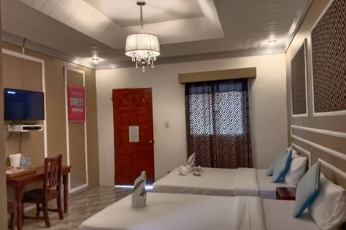 A hotel room with two beds, a TV, a desk, and a chandelier.