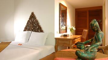A hotel room with a bed, a wooden desk, a chair, a decorative wall piece, and a statue.