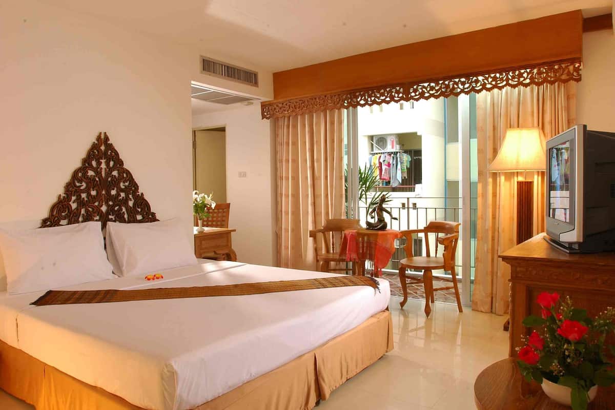 A hotel room with a large bed, a television, a desk with a lamp, and a view of a balcony with clothes hanging.