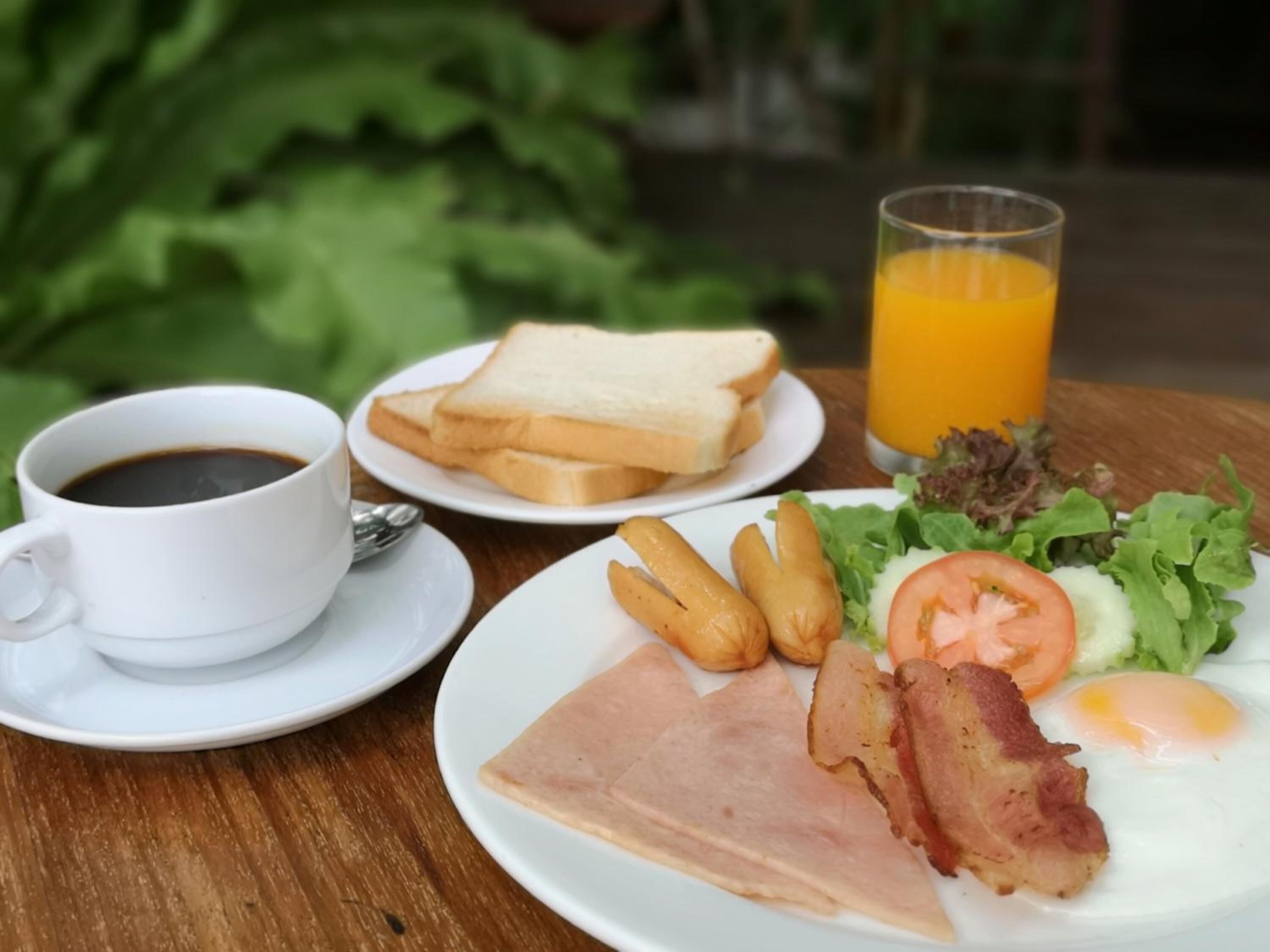 Un plato de desayuno con jamón, tocino, huevos y tostadas, una taza de café y un vaso de jugo de naranja sobre una mesa de madera.