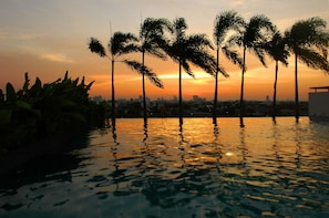 A sunset over a swimming pool with palm trees and a city skyline in the background. - Bansabai Hostel (Bangkok)