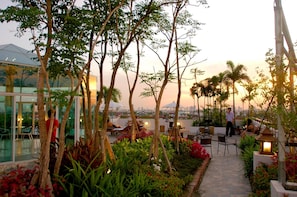 A rooftop garden with seating areas, trees, and a view of the city skyline. - Bansabai Hostel (Bangkok)