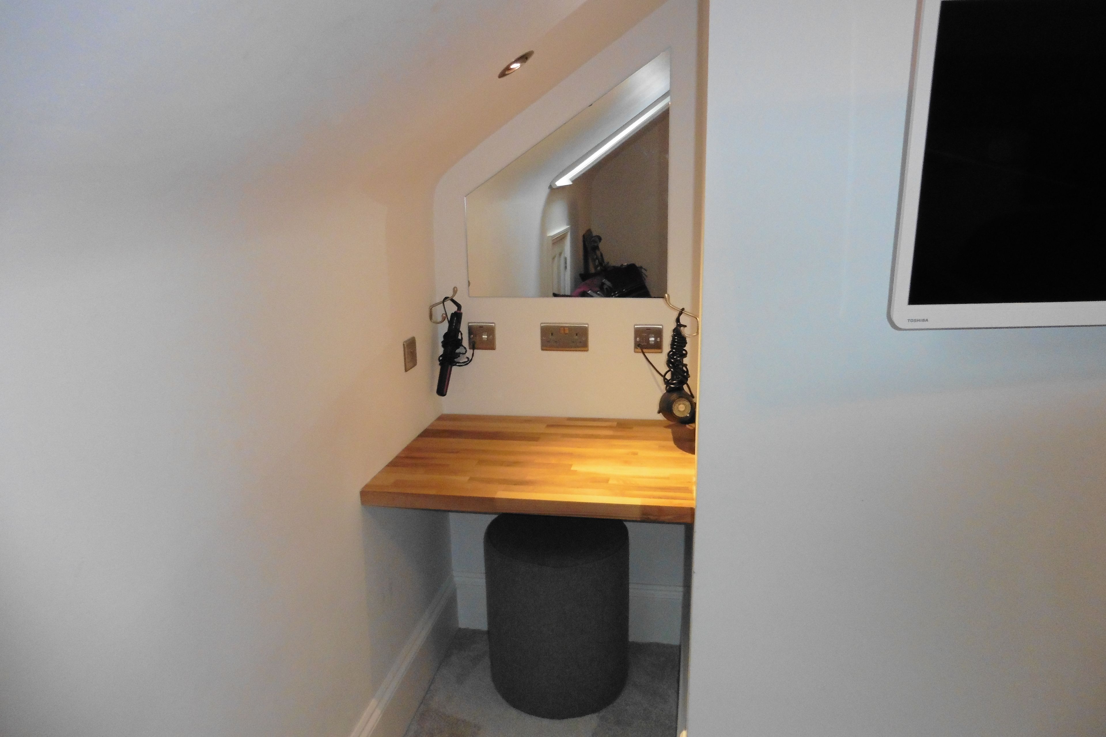 A small bathroom with a wooden vanity, a mirror, and a black trash bin.