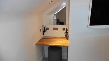 A small bathroom with a wooden vanity, a mirror, and a black trash bin.