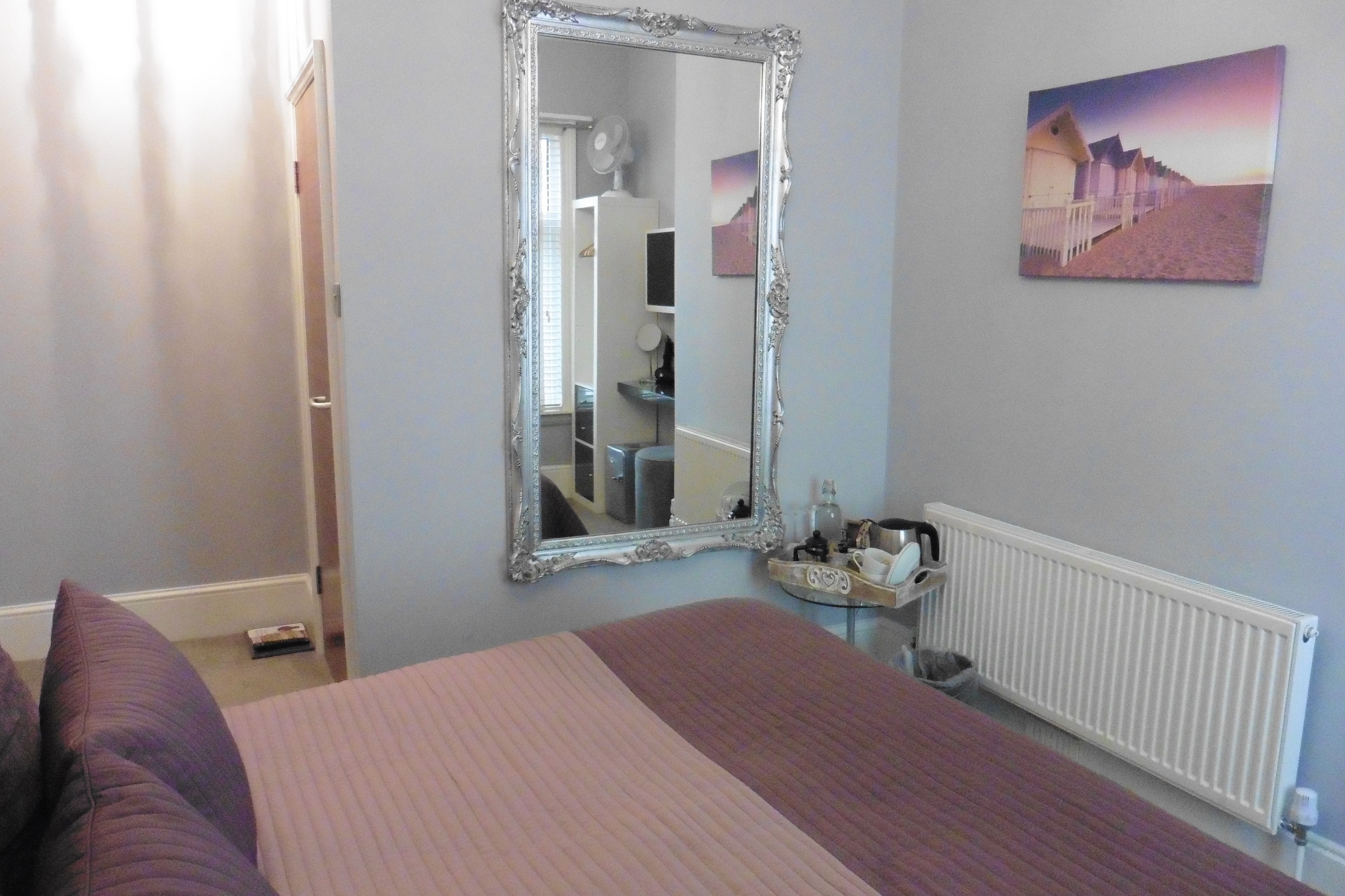 A bedroom with a large bed, a mirror, a radiator, and a painting on the wall.