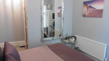 A bedroom with a large bed, a mirror, a radiator, and a painting on the wall.