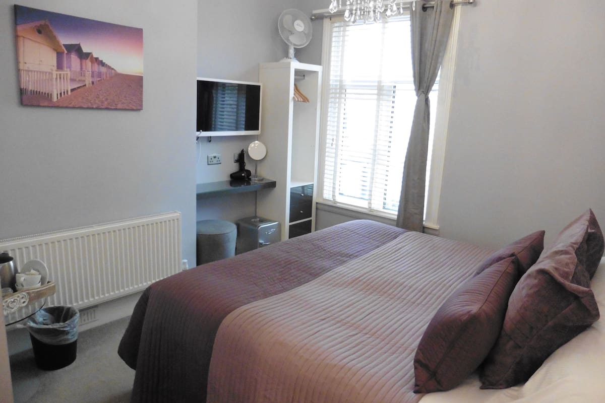 Un dormitorio con cama, televisor, cómoda y ventana con cortinas.
