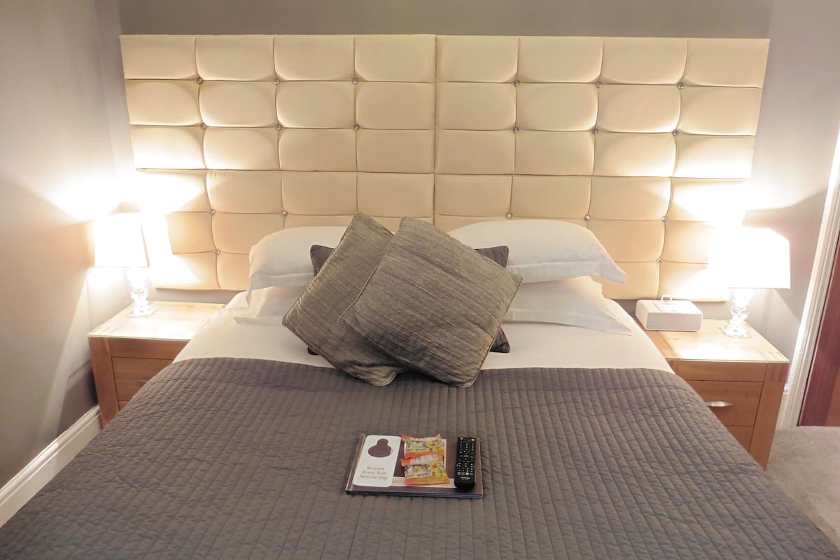 Una cama bien hecha con un cabecero capitonado, dos lámparas de noche y un control remoto sobre la cama.