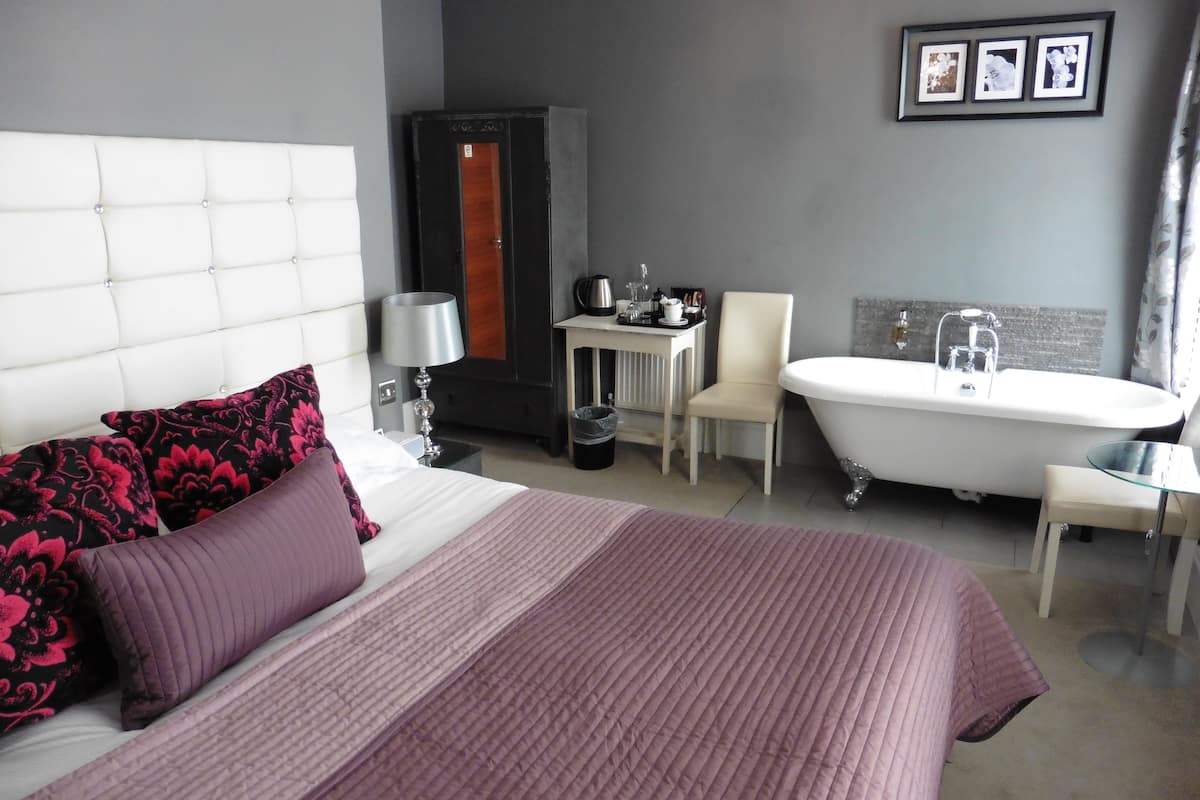 Habitación de hotel con una cama grande, zona de estar con una silla y una mesa, bañera y armario.