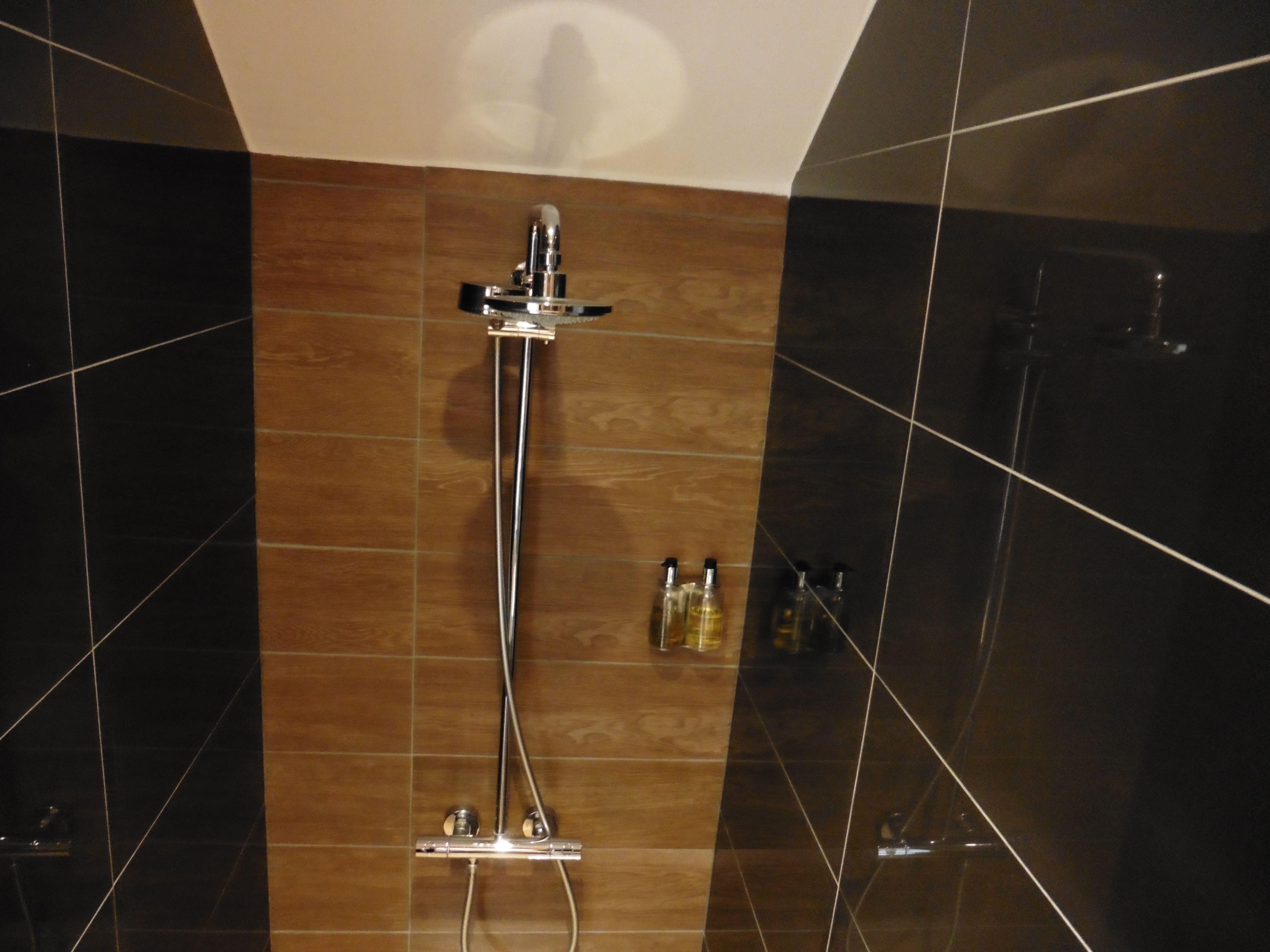 Une douche moderne avec un robinet et un panneau de commande chromés, le tout mis en valeur par un décor de carreaux de différentes nuances de marron, allant du foncé au clair.