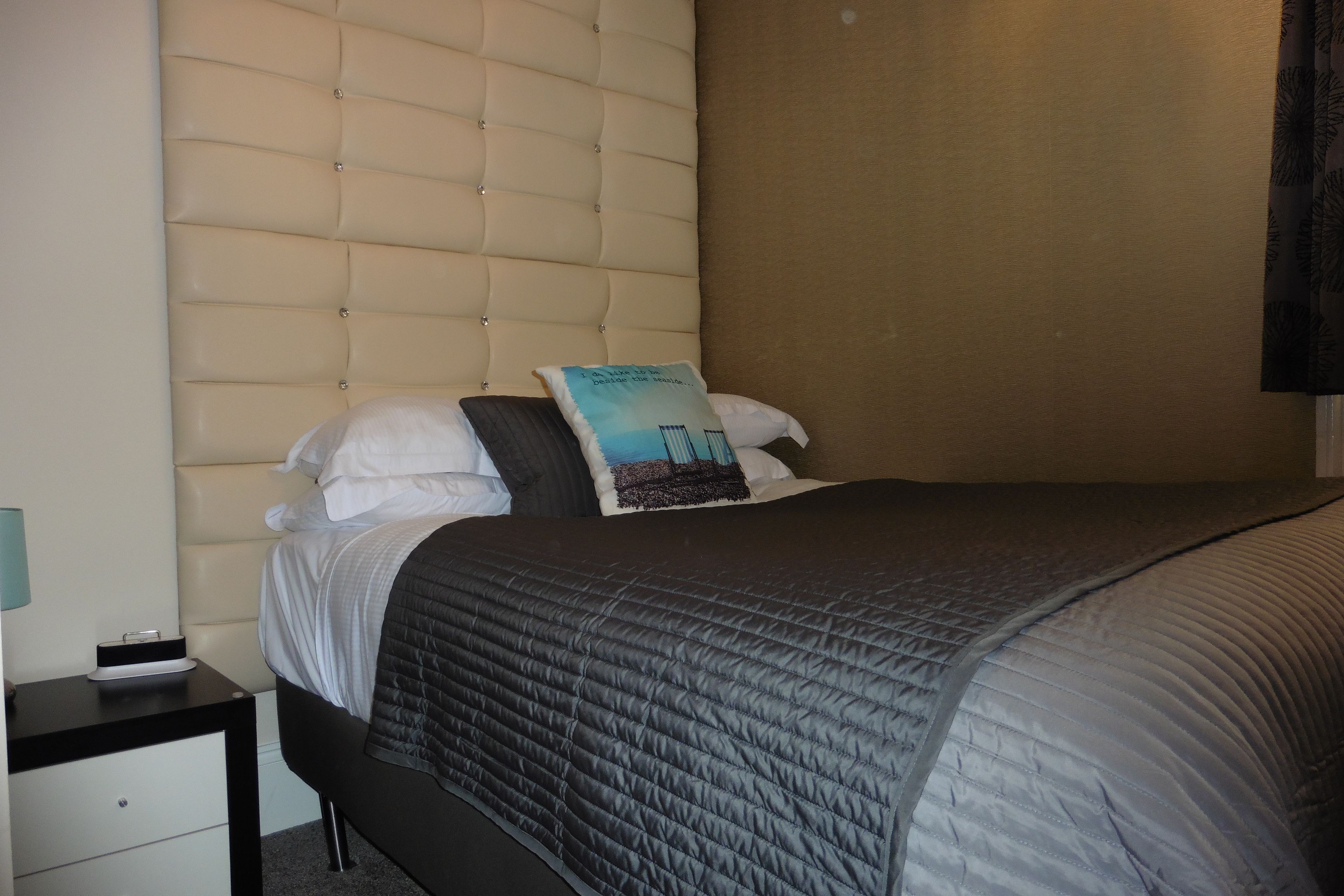 A neatly made bed with a quilted headboard, a bedside table with a lamp, and a pillow with a graphic design.