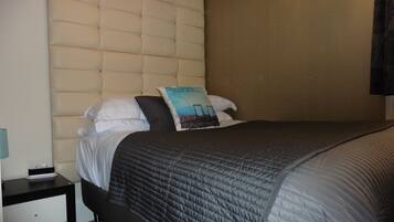 A neatly made bed with a quilted headboard, a bedside table with a lamp, and a pillow with a graphic design.