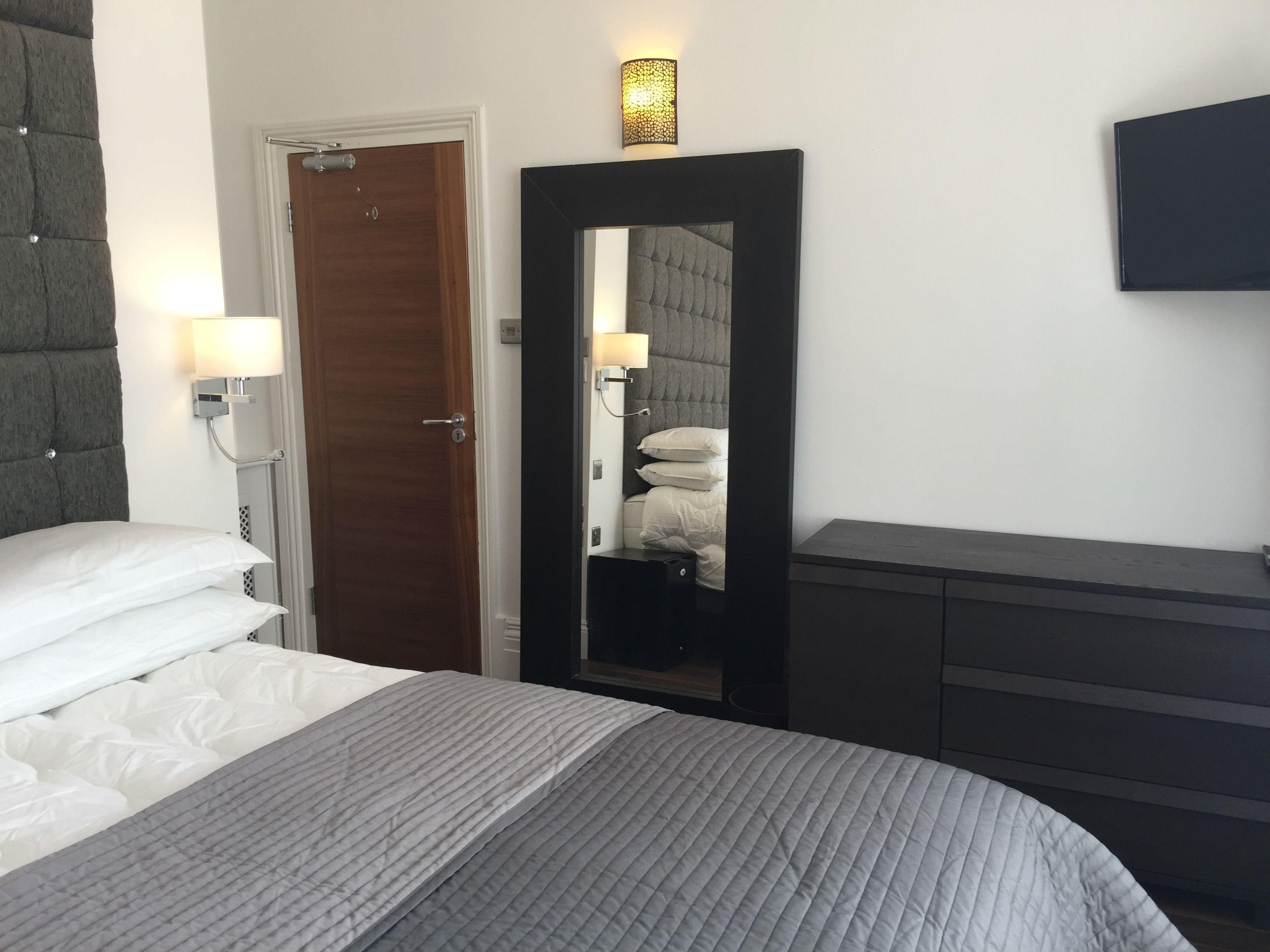 Une chambre d’hôtel avec un lit, une armoire, un miroir et une porte.