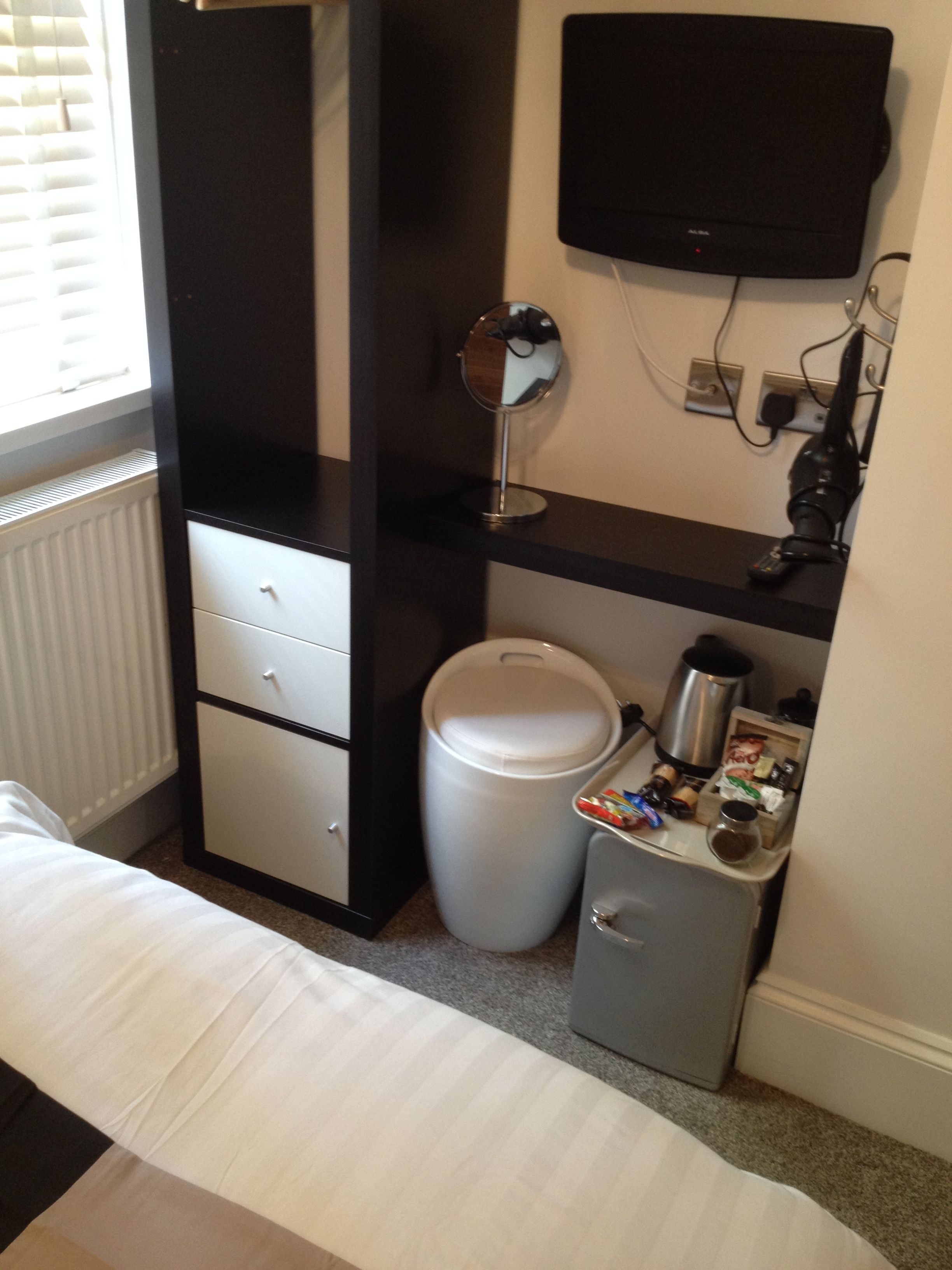 Une chambre compacte comprenant un lit, une petite table de chevet, une poubelle, une machine à café et un téléviseur fixé au mur.