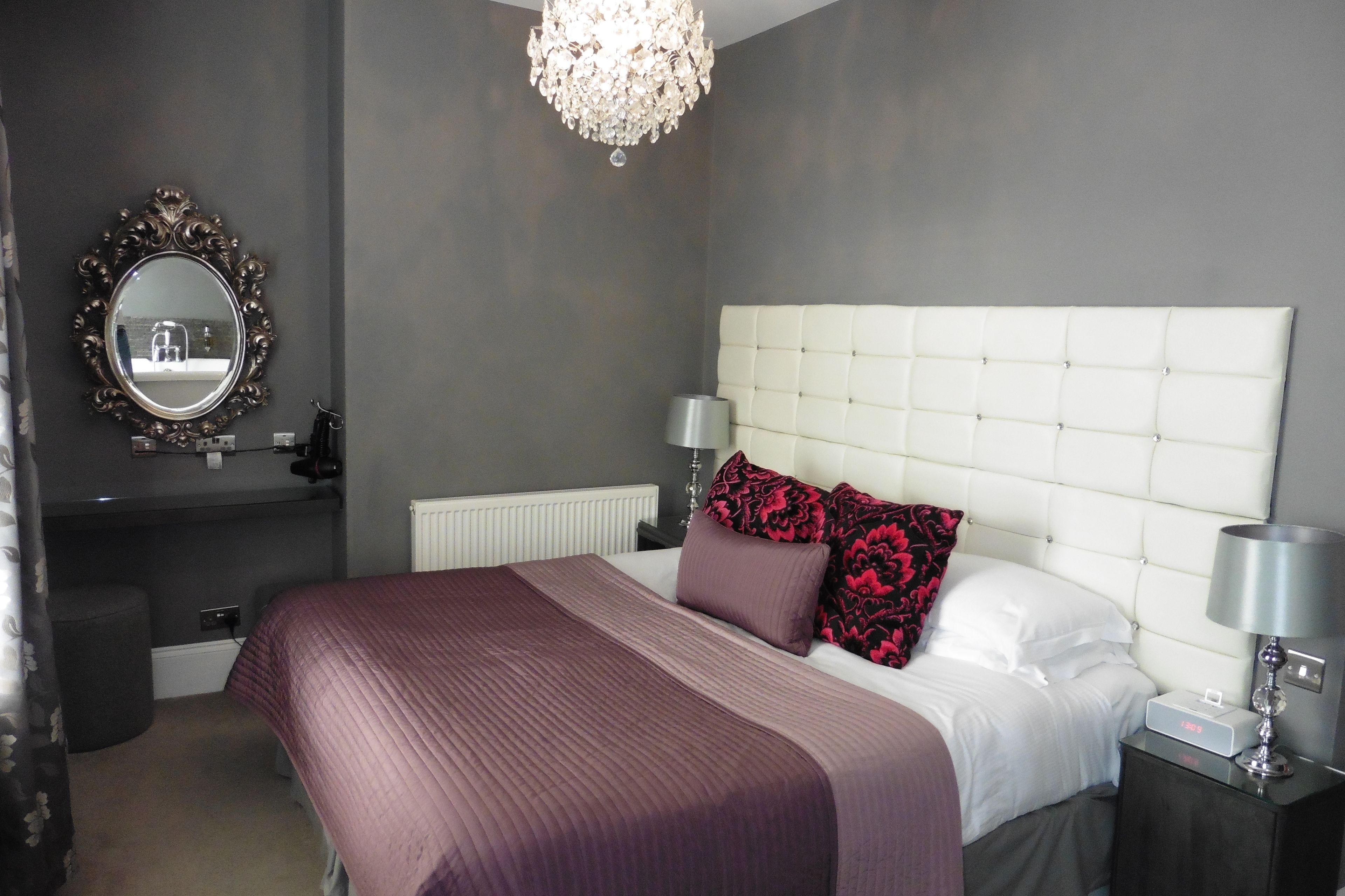 A bedroom with a large bed, a mirror, a chandelier, and a nightstand with a lamp.