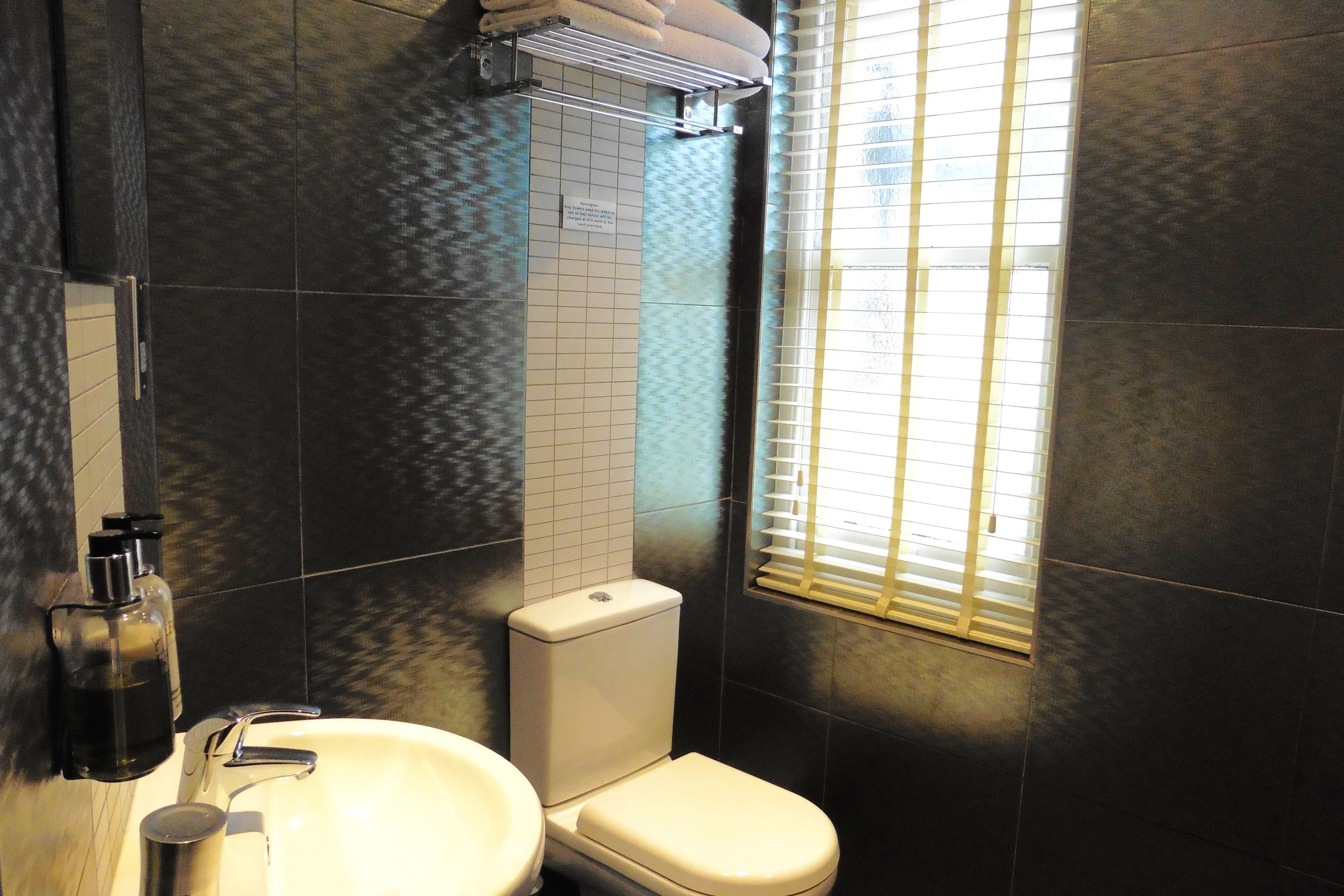 A modern bathroom with a white sink, a toilet, and a window with blinds.