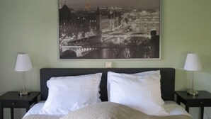 Habitación de hotel con cama, dos mesitas de noche y un cuadro grande en blanco y negro con una vista urbana.