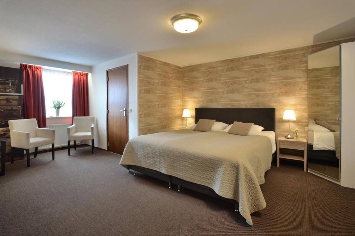 Ein Hotelzimmer mit einem großen Bett, zwei Nachttischen, einem Schreibtisch mit Stuhl und einem fenster mit Vorhängen.