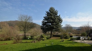 Un jardín cuidado con un gran árbol de coníferas, césped y un pequeño estanque.