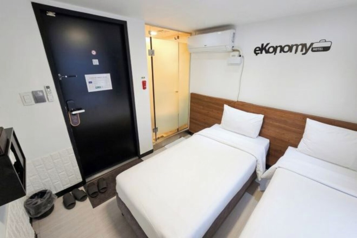 A hotel room with a bed, a wooden headboard, a wall-mounted air conditioner, and a door with a handle.