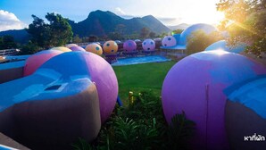 A series of large, colorful spherical structures in a resort setting with a pool and mountains in the background. - DNA Super Ozone Resort KhaoYai (Pak Chong)